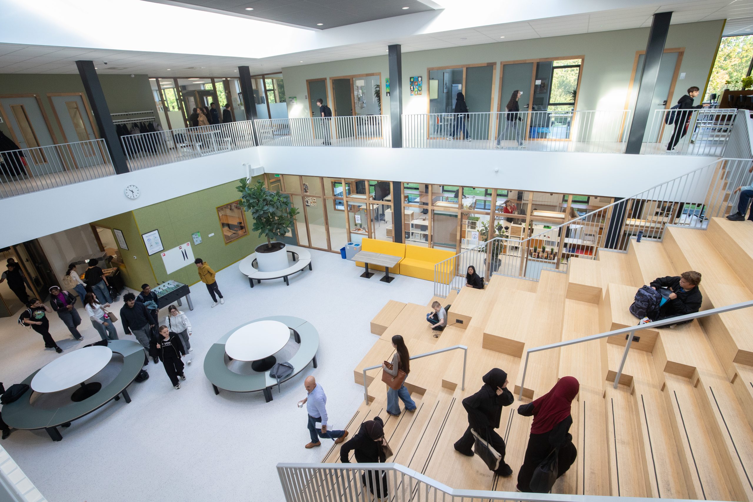 De aula van school met de houten tribunetrap, leerlingen lopen en zitten aan ronde tafels