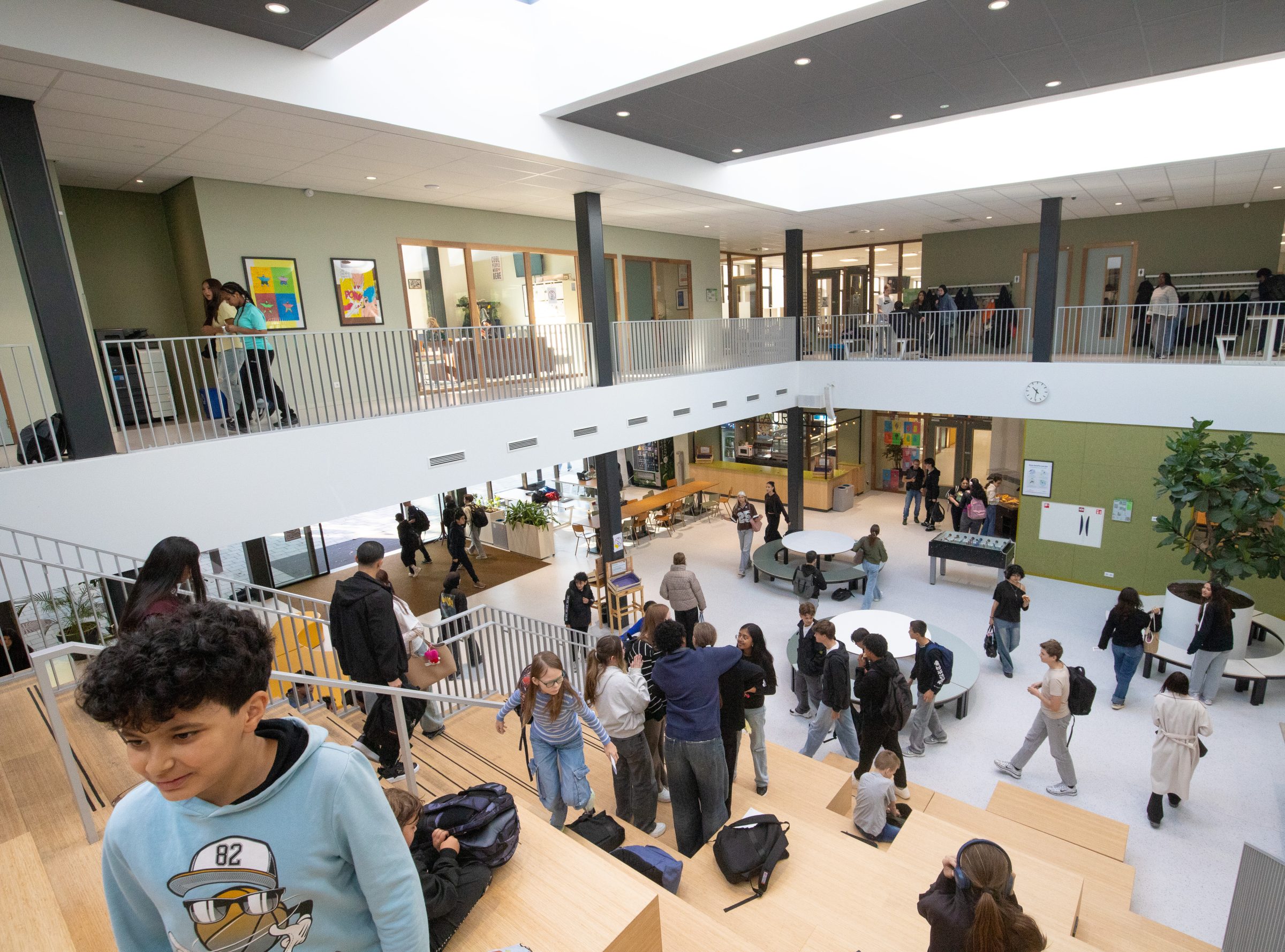 Leerlingen in de lichte aula met de houten tribunetrap en de galerij erboven