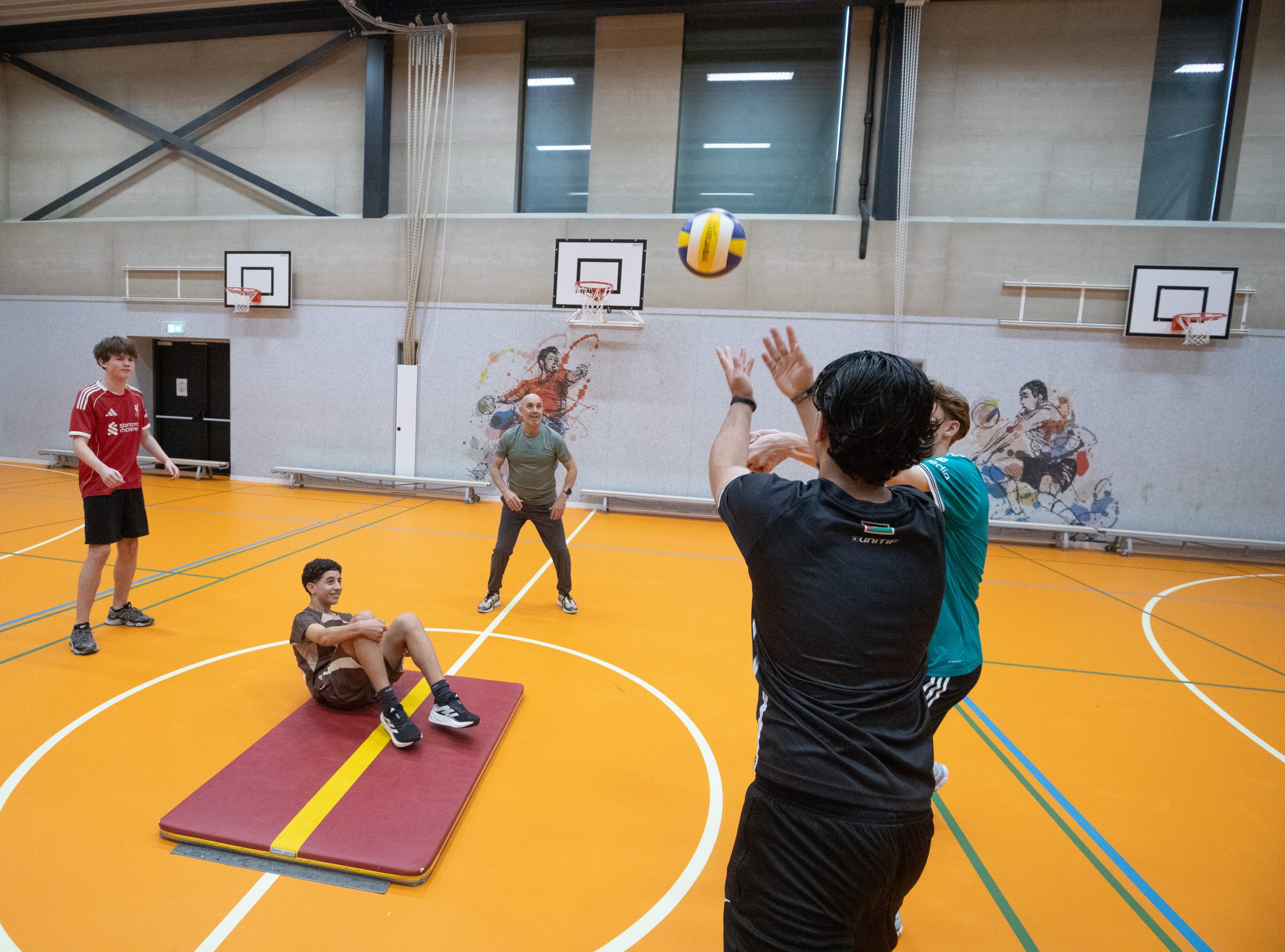 Leerlingen en docent spelen volleybal in de gymzaal
