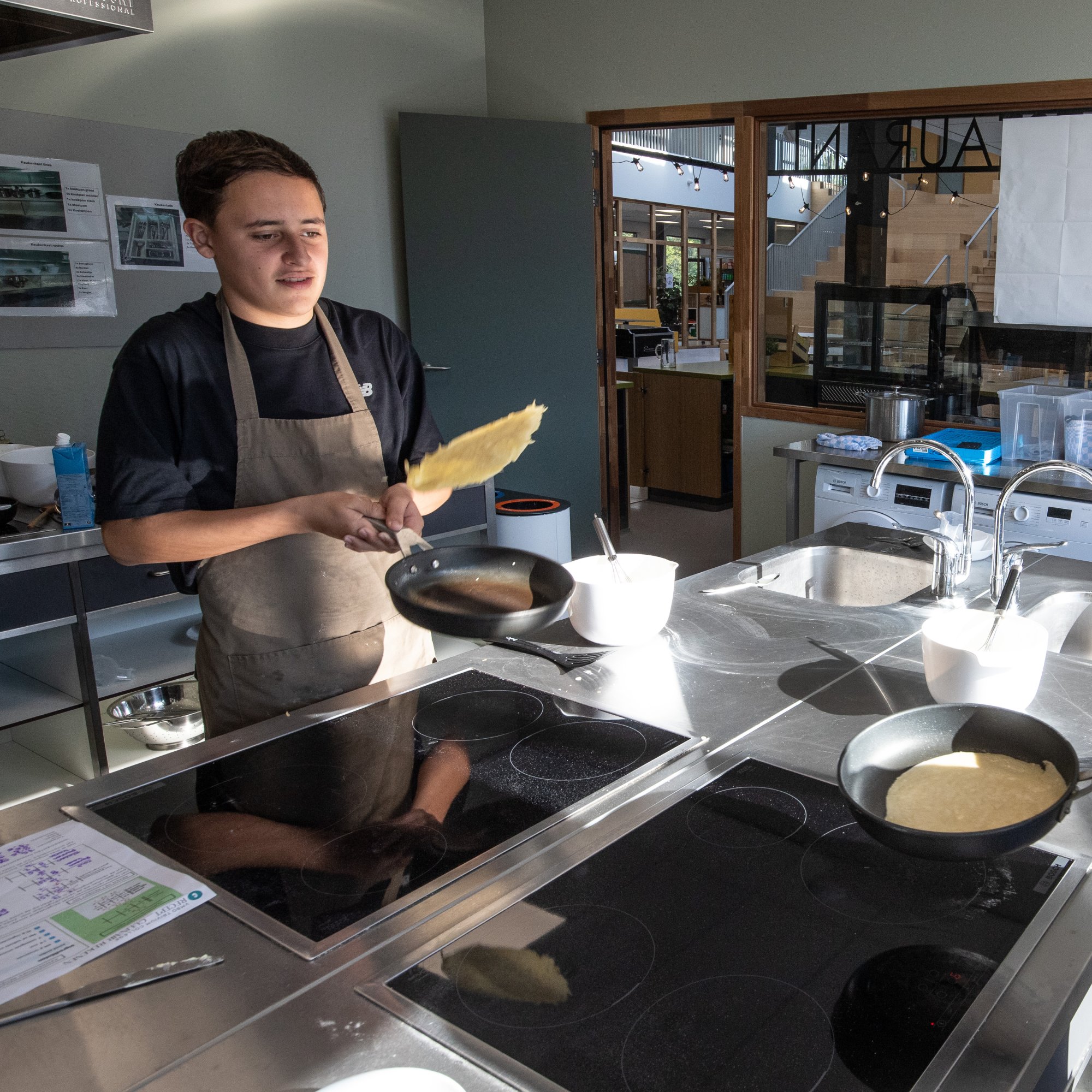 Een leerling draait een pannenkoek om in de schoolkeuken