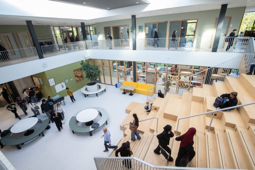 De lichte aula van Trivium College met de houten zittrap, ronde tafels en leerlingen op weg naar hun les